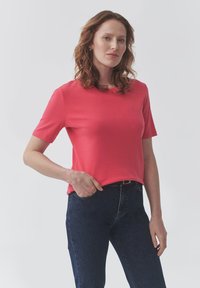 Korálový top s krátkým rukávem z hladk�ého materiálu, volnějšího střihu, s kulatým výstřihem, spárovaný s tmavě modrými džíny s slim fit střihem.