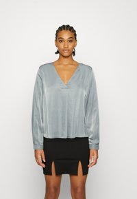 Blusa de seda cinza de mangas compridas com decote profundo em V e costuras franzidas, combinada com uma saia mini preta com duas fendas frontais.
