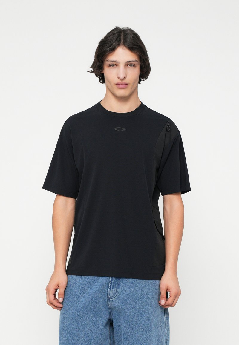 Μαύρο κοντομάνικο μπλουζάκι με στρογγυλή λαιμόκοψη, με ένα διακριτικό λογότυπο στο στήθος και υφασμάτινα πάνελ στο πλάι. Φτιαγμένο από ελαφρύ ύφασμα.