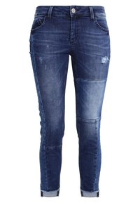 Džínové kalhoty v tmavě modré barvě s distressed designem, světlými vyblednutími, akcenty z nášivek a ohrnutými manžetami pro užší střih.