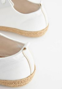 Biele espadrilky s textúrovanou jute podrážkou a béžovým prešívaním, s malým očkom na päte pre jednoduché obúvanie.