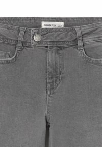 Los jeans de denim gris cuentan con un diseño clásico de cinco bolsillos, un cierre de botón metálico y detalles de costura visibles a lo largo de las costuras.