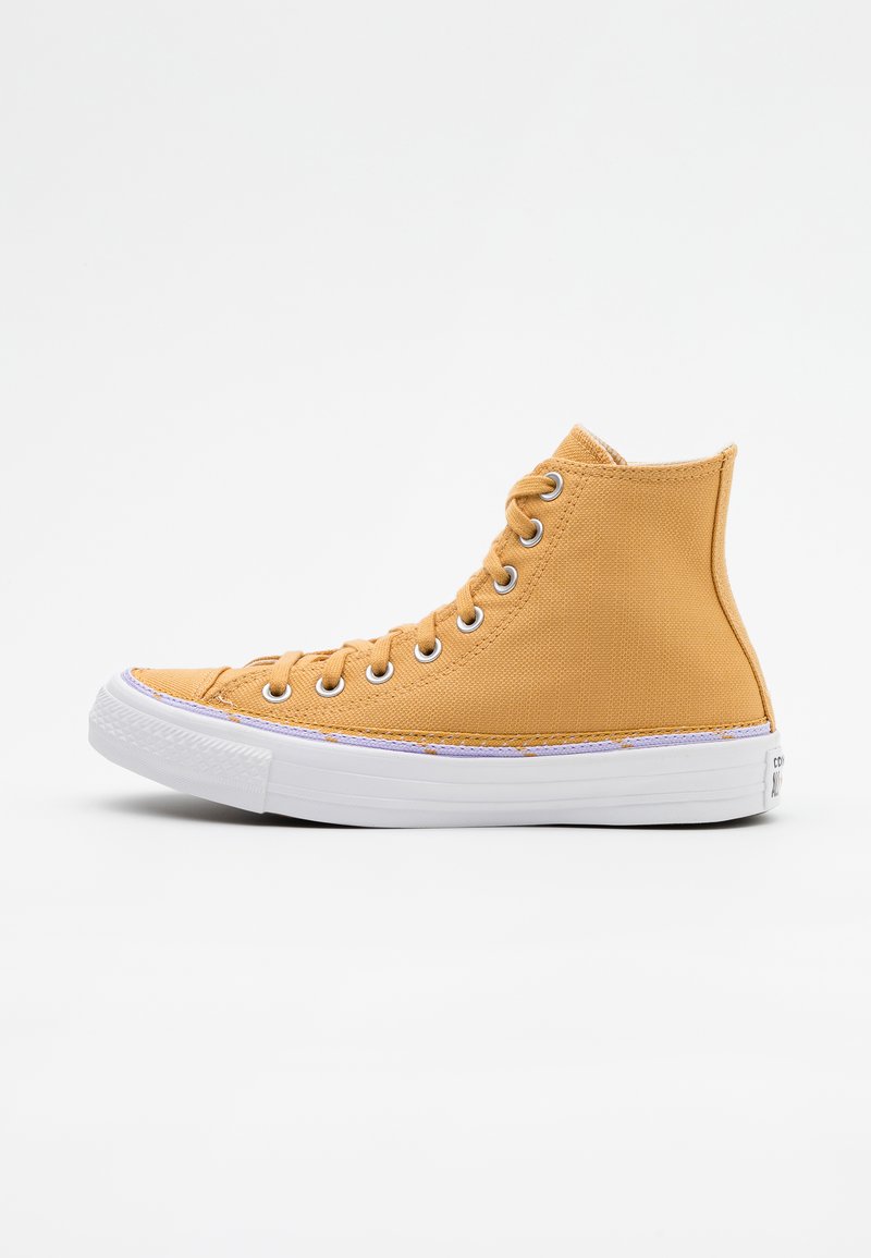 Wysokie trampki z płótna w musztardowym żółtym kolorze, z białymi gumowymi podeszwami, oczkami i szwami. Posiadają teksturowaną powierzchnię i widoczne sznurówki.