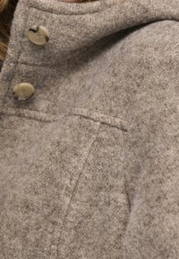 Cappotto in lana marrone caratterizzato da un morbido tessuto testurizzato con due grandi bottoni beige e un discreto dettaglio della tasca.