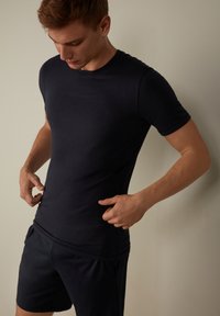 Námořnické tričko s krátkým rukávem z měkké tkaniny, přiléhavý střih, kulatý výstřih, spárované s tmavými šortkami, které vykazují hladkou strukturu a minimalistický styl.