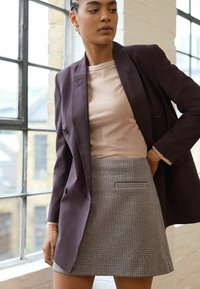 Mørk lilla blazer med to knapper, parret med en lys pink t-shirt og en grå houndstooth mini-nederdel med en sidelomme.