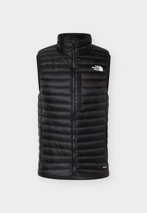 Svart quiltet ermeløs vest med frontglidelås, vertikal glidelåslomme på brystet, høy krage og hvit The North Face-logo foran.