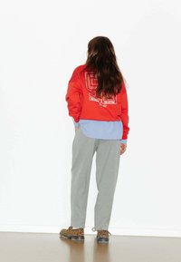 Sweatshirt surdimensionné rouge avec graphique blanc, chemise à boutons bleue en dessous, pantalon à rayures grises, et chaussures marron à imprimé léopard. Fond blanc.