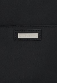 Czarny materiał o strukturze z metalową etykietą w kolorze srebrnym z napisem "Lancerto" przyszytą do powierzchni.