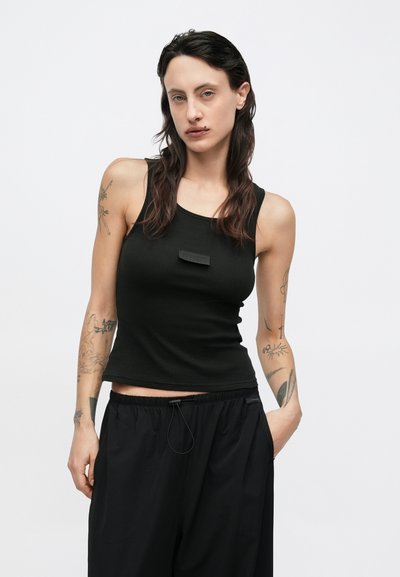 Svart ribbestrikket singlet med rund hals og liten logo på brystet. Kombinert med løse svarte bukser for et avslappet utseende.