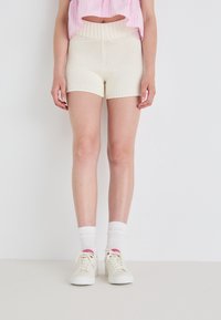 Gebreide ivoorkleurige shorts met een textuurpatroon, hoge elastische taille en een aansluitend ontwerp. Gepaard met witte sokken en lichtgekleurde sneakers.