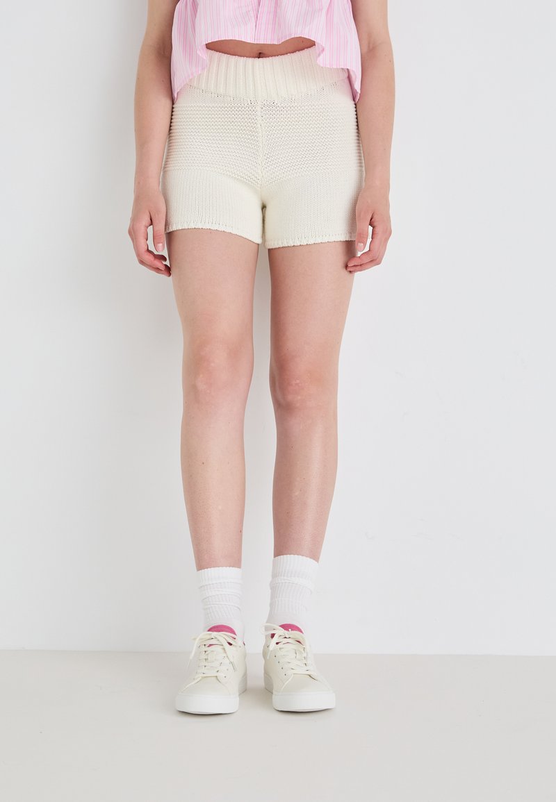 Gebreide ivoorkleurige shorts met een textuurpatroon, hoge elastische taille en een aansluitend ontwerp. Gepaard met witte sokken en lichtgekleurde sneakers.