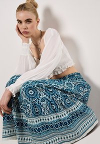 Vit texturerad crop-top med långa ärmar och volangkanter, kombinerad med en maxikjol i blått och vitt med blommönster.