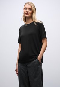 Zwart kortemouw t-shirt van zachte stof, met een ronde halslijn en een ontspannen pasvorm, gecombineerd met grijze gestructureerde broek.