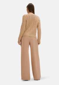 Beige Kabelstrickpullover mit langen Ärmeln und geripptem Saum, kombiniert mit hochwaistigen, weiten hellbraunen Hosen. Glatte Texturen und neutrale Farbtöne.