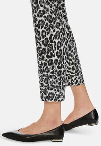 Schwarze spitze Ballerinas mit flachem Absatz, aus glattem Leder, kombiniert mit einer Hose im weißen und schwarzen Leopardenmuster.