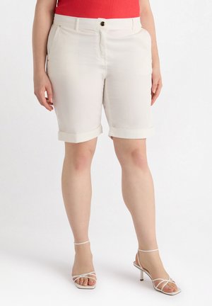 Weiße Shorts mit umgeschlagenem Saum, Vorderentaschen und Knopfverschluss, kombiniert mit weißen Riemchenschuhen. Glattes Baumwollmischgewebe.