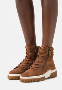 Bruna mockasin höga stövlar med en kraftig vit sula, har metalldragkedjefinter och snörning fram. Strukturert finish och hög topp-design.