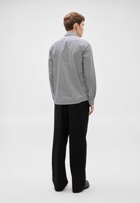 Ριγέ μακρυμάνικο πουκάμισο σε μαύρο και λευκό, με γιακά και μανσέτες με κουμπιά, συνδυασμένο με φαρδιά μαύρη παντελόνα. Ομαλή υφή υφάσματος.