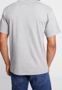 Grå bomullströja med kort ärm, rund halsringning och en slät textur, visad bakifrån med en nederkant som slutar strax ovanför midjan.