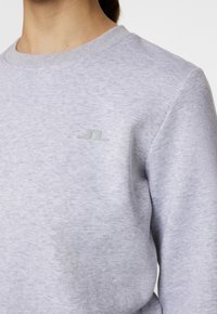 Ljusgrå sweatshirt i mjukt tyg med ribbad krage. Har en liten, texturerad logotyp på vänster bröstområde.