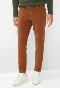 Pantaloni in corduroy marroni con vestibilità slim, caratterizzati da una texture a righe verticali. Abbinati a sneaker bianche e a un maglione verde scuro.