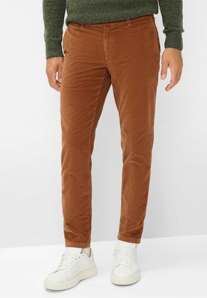 Brune fløjlbukser med slim fit, der har vertikal ribbet tekstur. Kombineret med hvide sneakers og en mørkegrøn sweater.