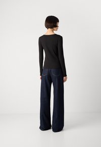Zwarte longsleeve top met een ronde halslijn, gecombineerd met wijde, donkere denim jeans, met subtiele stikdetails op de achterkant van de zakken.