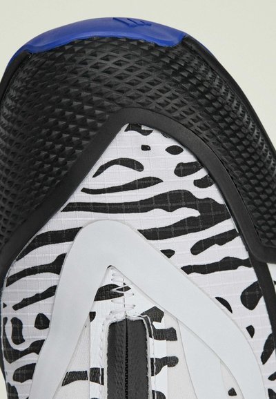 Čierne, biele a modré športové topánky s textúrovaným čiernym špičkovým obalom, bielym vrchom so zebrovým vzorom a štíhlym, moderným tvarom.