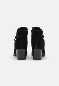 Stivali alla caviglia in suede nero con un tacco basso a blocco, dotati di una cerniera laterale e di una fibbia dorata su una cinghia regolabile.