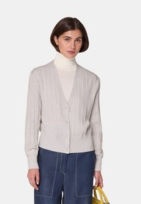 Hellgrauer Cardigan mit geripptem Textur, V-Ausschnitt, vorderen Knöpfen und einem enganliegenden Saum. Über einem weißen Rollkragenpullover gestylt und mit blauen Jeans kombiniert.