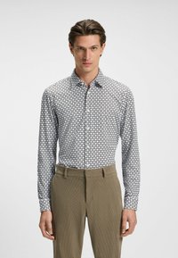 Witte langemouwen shirt met zwart geometrisch patroon, met knoopsluiting en een slim fit, gecombineerd met lichte beige broek.