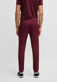 Burgundowe spodnie slim-fit z gładkiego materiału, z dwoma tylnymi kieszeniami, szwami z przodu, w połączeniu z czarnymi sneakersami.