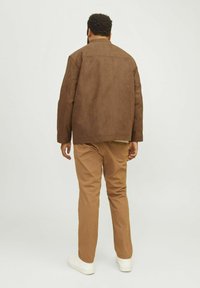 Chaqueta de ante marrón con un corte relajado, costuras visibles y un cuello alto, combinada con pantalones caqui y zapatillas blancas.