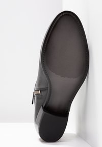 Schwarzer Lederschuh mit strukturiertem Obermaterial, seitlichem Reißverschlussdetail und einer glatten Gummisohle mit Rillen für besseren Halt.