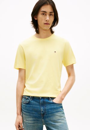 Yellow cotton t-shirt with short sleeves and a round neckline, featuring a small logo on the left chest. Worn with blue jeans.