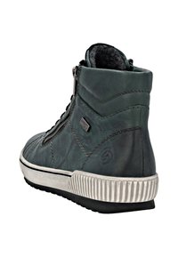 Basket haute vert foncé avec semelle en caoutchouc blanche, fermeture éclair sur le côté, lacets noirs, couture texturée et doublure en polaire visible à la cheville.