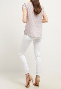 Blusa corta de manga corta en color rosa claro con un patrón de cuadros, combinada con jeans slim-fit blancos y sandalias de tacón alto beige.