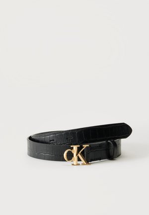 Ceinture noire texturée avec boucle dorée au logo CK, enroulée sur un fond blanc uni, sans personne ni objet supplémentaire.