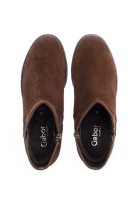 Hnědé nubukové kotníkové boty se hladkým povrchem, zipovým uzávěrem a kulatou špičkou. Interiér obsahuje detaily značky.