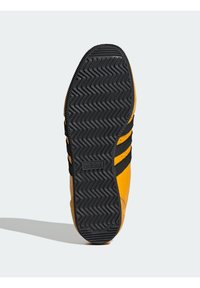 Orange och svart Adidas sneakersula med zigzagmönster och logotyp synlig i mitten, visad mot en enkel ljus bakgrund.