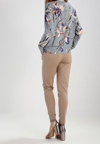 Lichtgrijze bloemenblouse met paarse en roze patronen, gecombineerd met beige op maat gemaakte broeken en metallic hoge hakken.