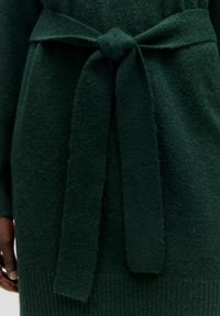 Grüner, gestrickter Pullover mit strukturiertem Finish, ausgestattet mit einem gebundenen Bund und geripptem Saum. Weicher Stoff mit gemütlicher Optik.