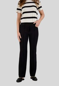 Pantaloni neri su misura con una vita testurizzata, dotati di tasche frontali e dettagli di cucitura discreti, abbinati a un top a righe bianche e nere.
