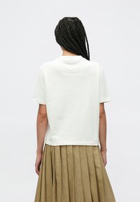 Λευκό βαμβακερό μπλουζάκι με άνετη εφαρμογή, κοντά μανίκια και στρογγυλή λαιμόκοψη, σε συνδυασμό με μια μπεζ πλισέ φούστα. Μινιμαλιστικός σχεδιασμός.