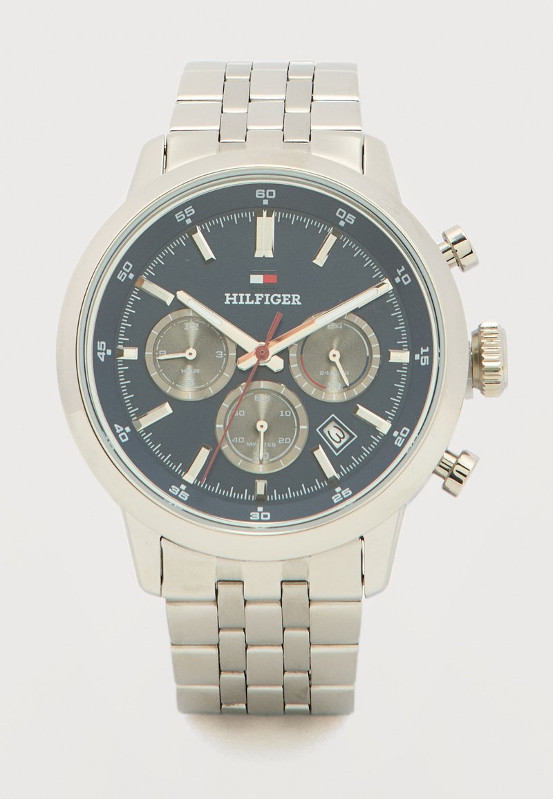 Ασημένιο μεταλλικό ρολόι χειρός με μαύρο καντράν, τρεις υποκαντράν, ένδειξη ημερομηνίας και λογότυπο "Hilfiger", με μπρασελέ σύνδεσης.