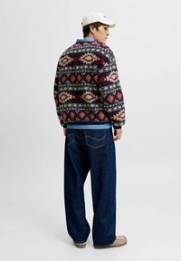 Wollen patroontrui in marineblauw, bordeauxrood en crème, gecombineerd met losse donkere spijkerbroek en beige schoenen, met daaronder een lichtblauw shirt.