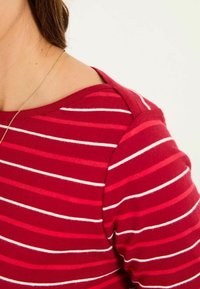 Red and white striped shirt with a soft texture, featuring a rounded neckline and short sleeves. Notable shoulder detail.