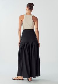 Gonna lunga nera con orlo arricciato, realizzata in un tessuto leggero. Abbinata a un top a canottiera beige a costine e sandali neri piatti.