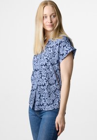 Blusa a maniche corte blu navy con un motivo floreale in azzurro. Presenta un collo a V e una vestibilità rilassata. Abbinata a jeans blu.